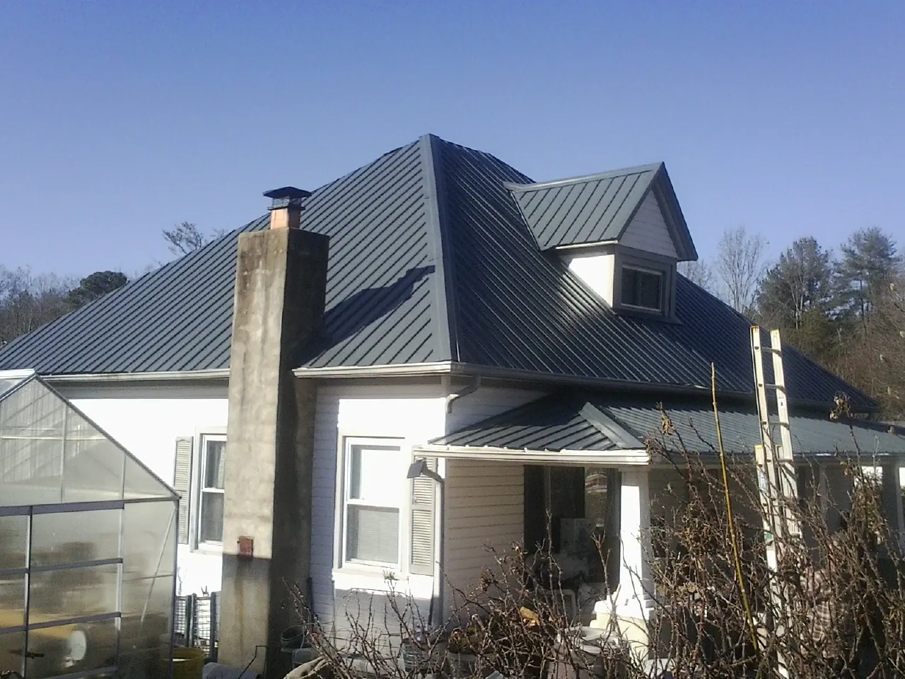 Dark blue standing seam metal roof on a white farmhouse with dormer — Slate & Tile Roof Repair by Roofing Brothers in Belle