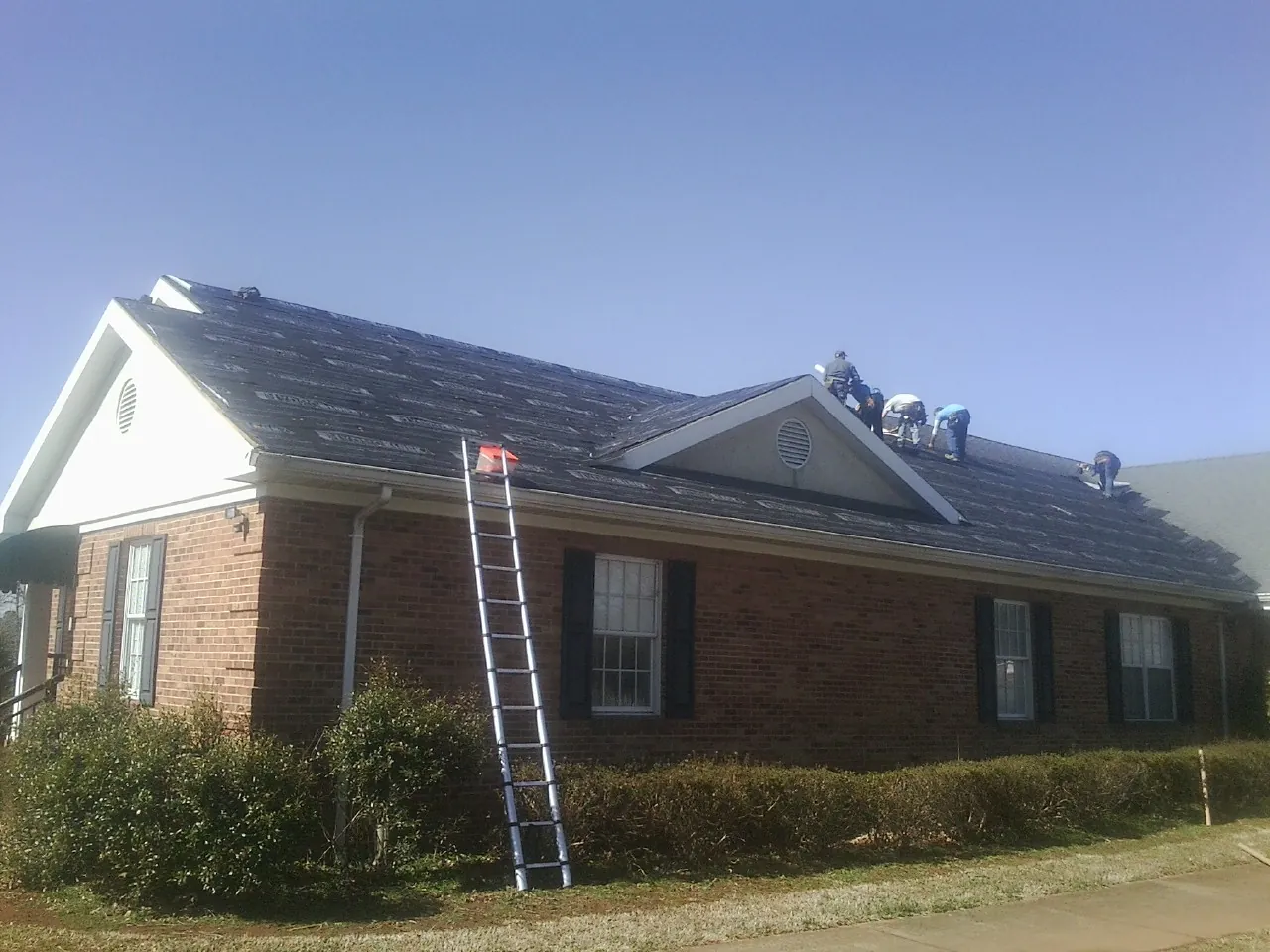 Crew tearing shingles off a brick ranch roof with a ladder set — Emergency Roof Repair work by our crew in Belle