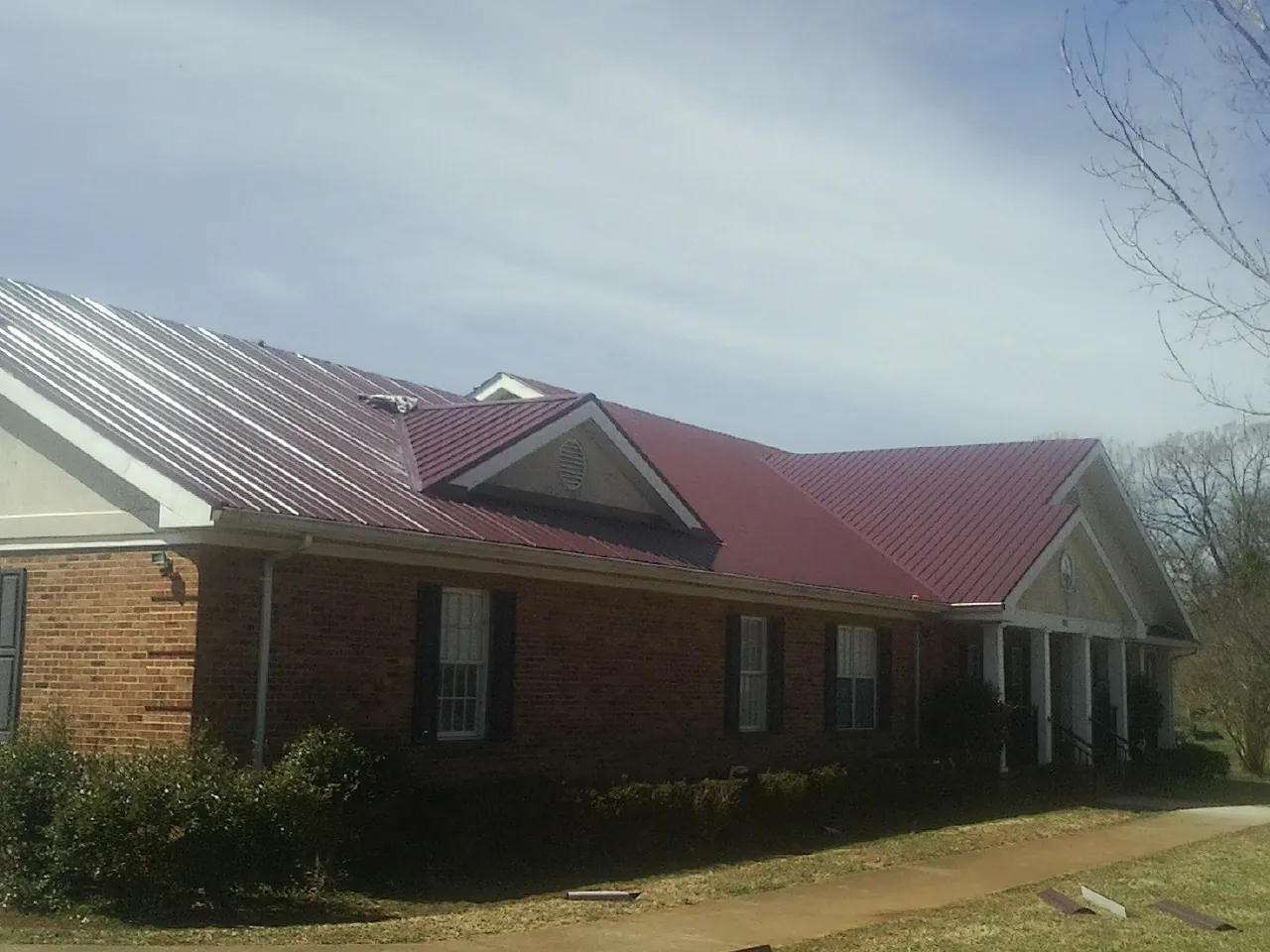 Red metal roof with gabled entries on a long brick building, from a Hail Damage Roof Repair job in Belle