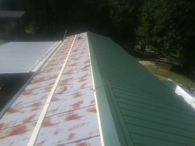 Old rusted panels beside newly installed green metal roofing — Wind Damage Roof Repair by Roofing Brothers in Belle
