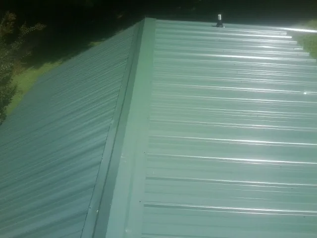 New green metal panels meeting at the ridge of a roof — Flat Roof Repair work by our crew in Belle