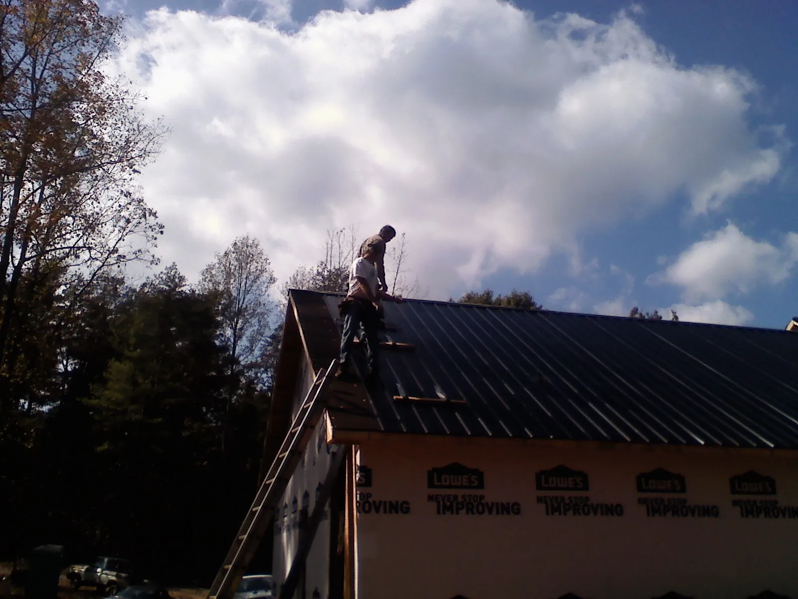 Roofer fastening dark metal panels high against a cloudy sky, from a Roof Inspection job in Belle