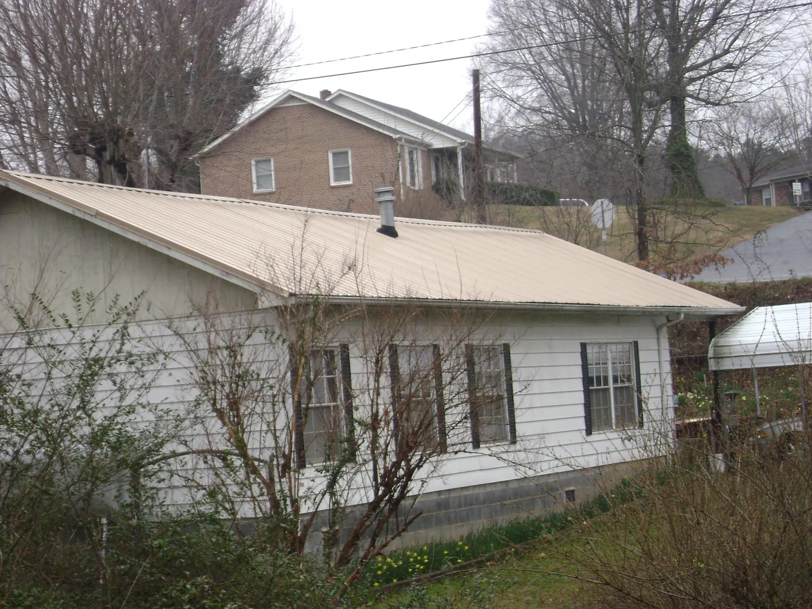 Tan metal roof on a white sided house set into a hillside — Commercial Roofing by Roofing Brothers in Belle